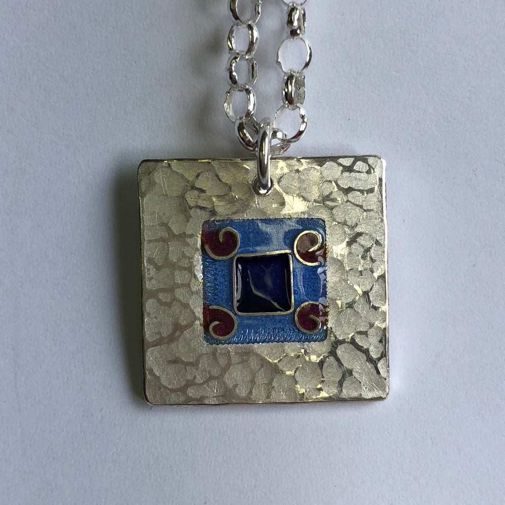 Pendant, blue on blue square with 4 red koru's